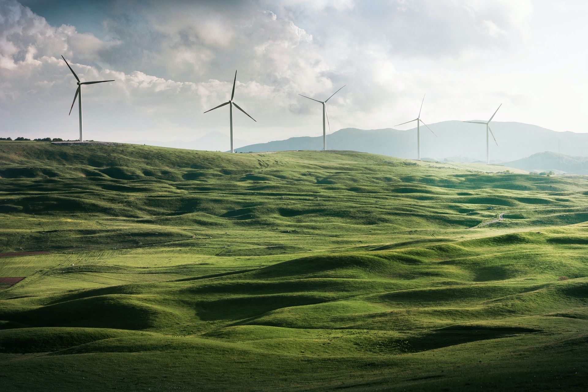 Bild einer grünen Landschaft mit Bergen und Windrädern am Horizont.